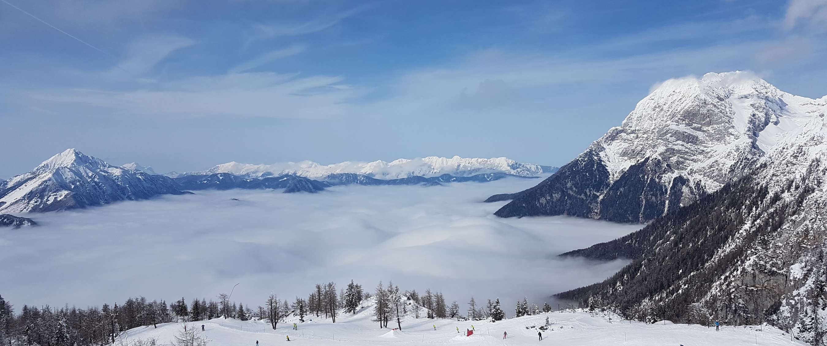 Skiërs op een piste met uitzicht op besneeuwde bergtoppen die boven de wolken uitsteken in Krvavec.