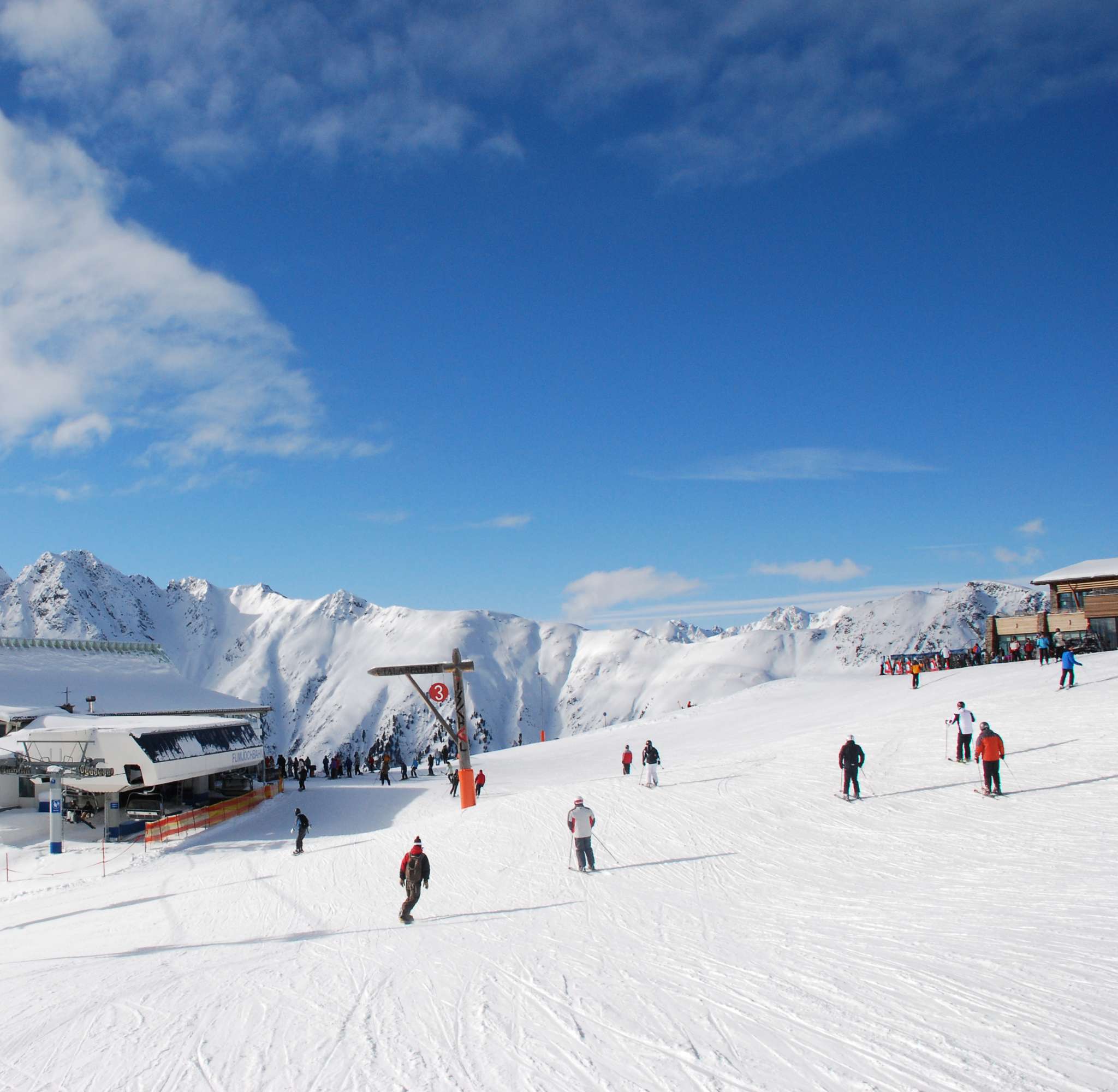 Een skiresort met een groot gebouw en skiërs op een brede, besneeuwde helling in Ischgl.